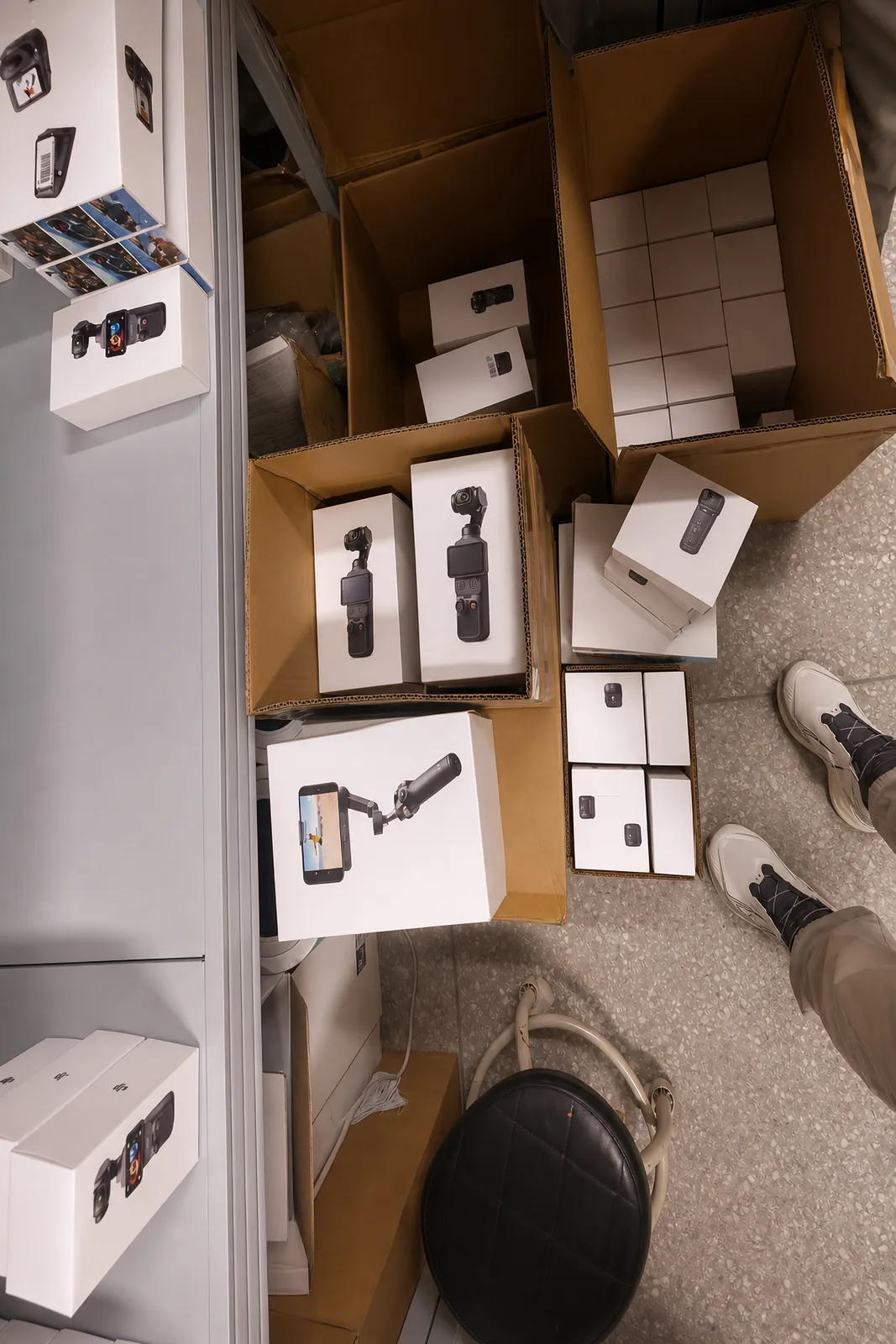 Open cartons of boxed DJI Osmo Pocket cameras and phone gimbals on the stock-room floor, seen from above